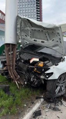 Şehir yolundaki bir kazadan sonra ağır hasar görmüş beyaz bir sedan. Araba bir direğe çarptı, ön kısmı parçalandı, kaput açık. Kaza, yol tehlikesi ve sigorta kavramı.