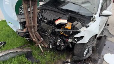 Şehir yolundaki bir kazadan sonra ağır hasar görmüş beyaz bir sedan. Araba bir direğe çarptı, ön kısmı parçalandı, kaput açık. Kaza, yol tehlikesi ve sigorta kavramı.