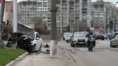Şehir yolundaki bir kazadan sonra ağır hasar görmüş beyaz bir sedan. Araba bir direğe çarptı, ön kısmı parçalandı, kaput açık. Kaza, yol tehlikesi ve sigorta kavramı.