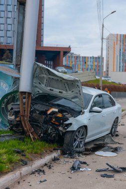 Şehir yolundaki bir kazadan sonra ağır hasar görmüş beyaz bir sedan. Araba bir direğe çarptı, ön kısmı parçalandı, kaput açık. Kaza, yol tehlikesi ve sigorta kavramı.