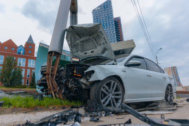 Şehir yolundaki bir kazadan sonra ağır hasar görmüş beyaz bir sedan. Araba bir direğe çarptı, ön kısmı parçalandı, kaput açık. Kaza, yol tehlikesi ve sigorta kavramı.