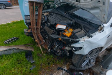 Şehir yolundaki bir kazadan sonra ağır hasar görmüş beyaz bir sedan. Araba bir direğe çarptı, ön kısmı parçalandı, kaput açık. Kaza, yol tehlikesi ve sigorta kavramı.