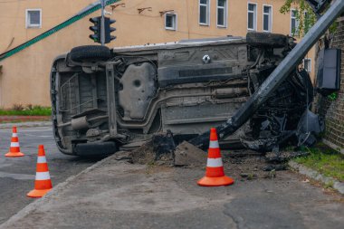 Devrilmiş bir araba yolun kenarında yan yatar. Bir araba kazasının olduğu yer. Arabada ciddi hasar var. Detaylar, yakın plan. Bir direğe çarpmış..