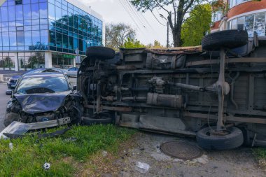 Bir şehir caddesinde iki arabalık bir kaza meydana geldi, bunlardan biri devrildi. Kırık farlar, yamuk bir kaput, kırık bir tampon ve cam kırıkları görülebilir.. 