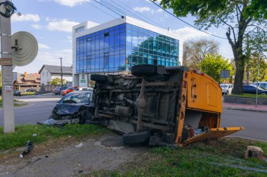 Bir şehir caddesinde iki arabalık bir kaza meydana geldi, bunlardan biri devrildi. Kırık farlar, yamuk bir kaput, kırık bir tampon ve cam kırıkları görülebilir.. 
