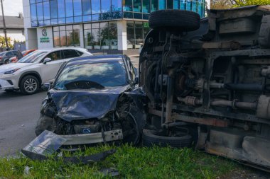 Bir şehir caddesinde iki arabalık bir kaza meydana geldi, bunlardan biri devrildi. Kırık farlar, yamuk bir kaput, kırık bir tampon ve cam kırıkları görülebilir.. 