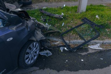 Bir şehir caddesinde iki arabalık bir kaza meydana geldi, bunlardan biri devrildi. Kırık farlar, yamuk bir kaput, kırık bir tampon ve cam kırıkları görülebilir.. 