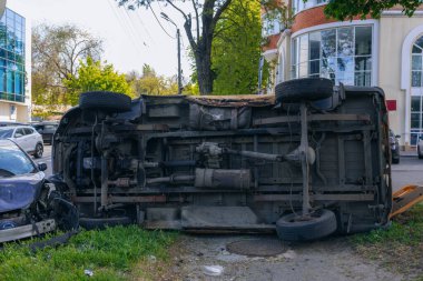 Bir şehir caddesinde iki arabalık bir kaza meydana geldi, bunlardan biri devrildi. Kırık farlar, yamuk bir kaput, kırık bir tampon ve cam kırıkları görülebilir.. 