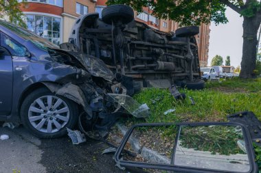 Bir şehir caddesinde iki arabalık bir kaza meydana geldi, bunlardan biri devrildi. Kırık farlar, yamuk bir kaput, kırık bir tampon ve cam kırıkları görülebilir.. 