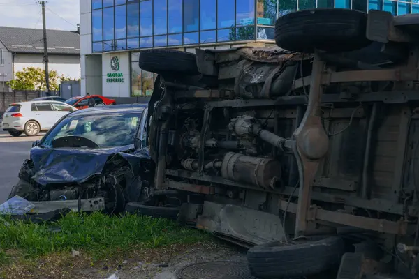 Bir şehir caddesinde iki arabalık bir kaza meydana geldi, bunlardan biri devrildi. Kırık farlar, yamuk bir kaput, kırık bir tampon ve cam kırıkları görülebilir.. 