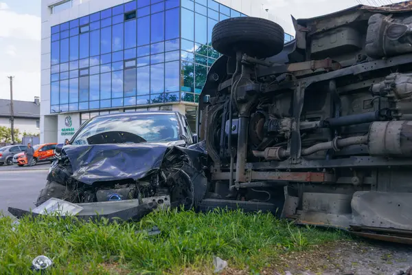 Bir şehir caddesinde iki arabalık bir kaza meydana geldi, bunlardan biri devrildi. Kırık farlar, yamuk bir kaput, kırık bir tampon ve cam kırıkları görülebilir.. 