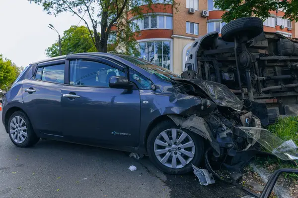 Bir şehir caddesinde iki arabalık bir kaza meydana geldi, bunlardan biri devrildi. Kırık farlar, yamuk bir kaput, kırık bir tampon ve cam kırıkları görülebilir.. 
