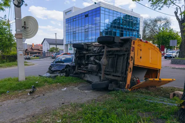 Bir şehir caddesinde iki arabalık bir kaza meydana geldi, bunlardan biri devrildi. Kırık farlar, yamuk bir kaput, kırık bir tampon ve cam kırıkları görülebilir.. 