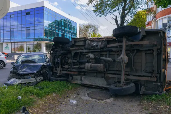 Bir şehir caddesinde iki arabalık bir kaza meydana geldi, bunlardan biri devrildi. Kırık farlar, yamuk bir kaput, kırık bir tampon ve cam kırıkları görülebilir.. 