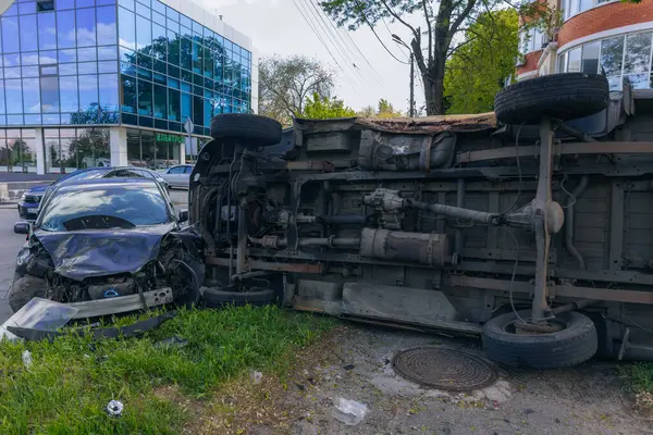 Bir şehir caddesinde iki arabalık bir kaza meydana geldi, bunlardan biri devrildi. Kırık farlar, yamuk bir kaput, kırık bir tampon ve cam kırıkları görülebilir.. 