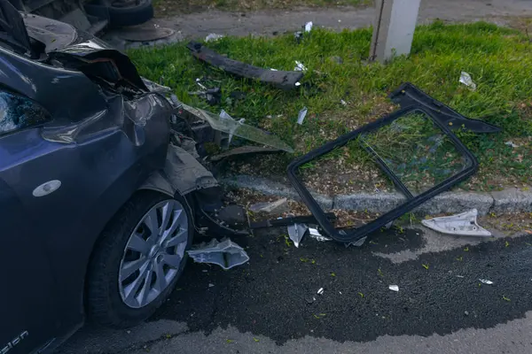 Bir şehir caddesinde iki arabalık bir kaza meydana geldi, bunlardan biri devrildi. Kırık farlar, yamuk bir kaput, kırık bir tampon ve cam kırıkları görülebilir.. 