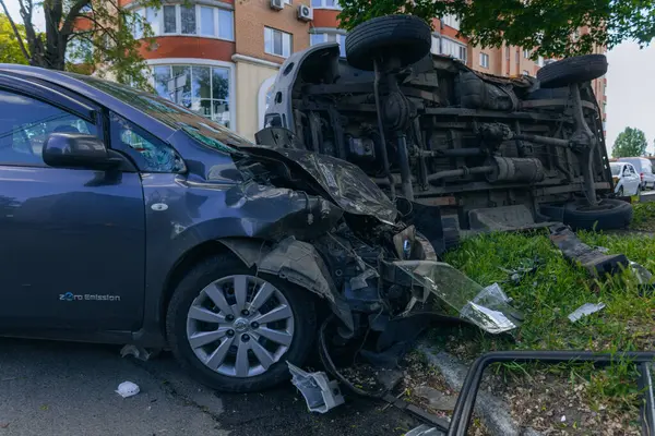 Bir şehir caddesinde iki arabalık bir kaza meydana geldi, bunlardan biri devrildi. Kırık farlar, yamuk bir kaput, kırık bir tampon ve cam kırıkları görülebilir.. 