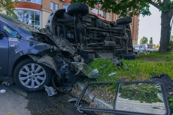 Bir şehir caddesinde iki arabalık bir kaza meydana geldi, bunlardan biri devrildi. Kırık farlar, yamuk bir kaput, kırık bir tampon ve cam kırıkları görülebilir.. 