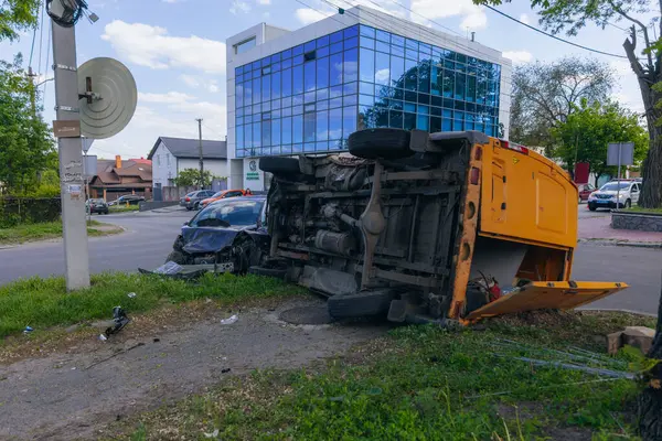 Bir şehir caddesinde iki arabalık bir kaza meydana geldi, bunlardan biri devrildi. Kırık farlar, yamuk bir kaput, kırık bir tampon ve cam kırıkları görülebilir.. 