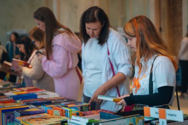 Kitapçıya ya ya da kitap fuarına gelip kitap seçiyor. Alışveriş ve okuma. Kütüphane. Kitap festivali. Kültürel etkinlik.