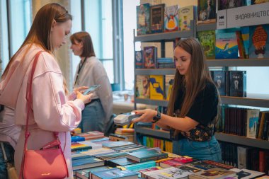 Kitapçıya ya ya da kitap fuarına gelip kitap seçiyor. Alışveriş ve okuma. Kütüphane. Kitap festivali. Kültürel etkinlik.