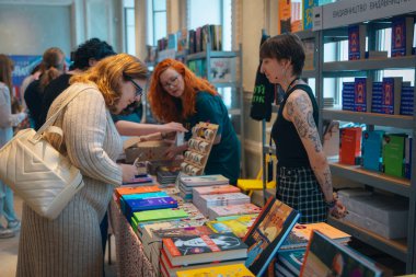 Kitapçıya ya ya da kitap fuarına gelip kitap seçiyor. Alışveriş ve okuma. Kütüphane. Kitap festivali. Kültürel etkinlik.
