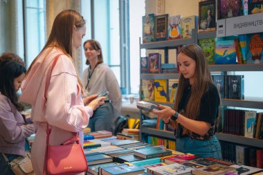 Kitapçıya ya ya da kitap fuarına gelip kitap seçiyor. Alışveriş ve okuma. Kütüphane. Kitap festivali. Kültürel etkinlik.