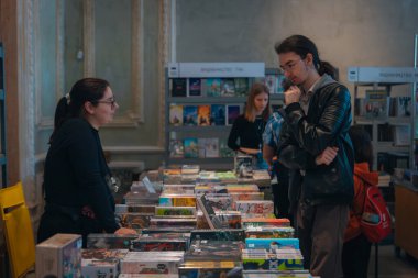 Kitapçıya ya ya da kitap fuarına gelip kitap seçiyor. Alışveriş ve okuma. Kütüphane. Kitap festivali. Kültürel etkinlik.