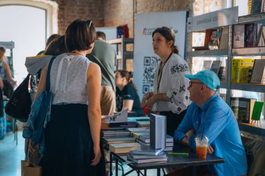 Kitapçıya ya ya da kitap fuarına gelip kitap seçiyor. Alışveriş ve okuma. Kütüphane. Kitap festivali. Kültürel etkinlik.
