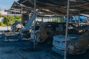 Kül ve çamur kaplı yanmış cesetlerde bükülmüş metal ve erimiş yapılar görülüyor. Arabanın içi mahvolmuş. Askeri çatışma ve bombardıman sonucu. Yıkılmış otopark.