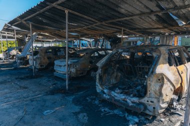 Kül ve çamur kaplı yanmış cesetlerde bükülmüş metal ve erimiş yapılar görülüyor. Arabanın içi mahvolmuş. Askeri çatışma ve bombardıman sonucu. Yıkılmış otopark.