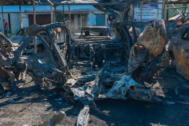 Kül ve çamur kaplı yanmış cesetlerde bükülmüş metal ve erimiş yapılar görülüyor. Arabanın içi mahvolmuş. Askeri çatışma ve bombardıman sonucu. Yıkılmış otopark.