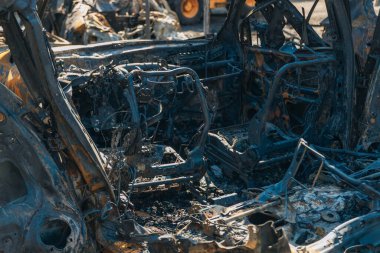 Kül ve çamur kaplı yanmış cesetlerde bükülmüş metal ve erimiş yapılar görülüyor. Arabanın içi mahvolmuş. Askeri çatışma ve bombardıman sonucu. Yıkılmış otopark.