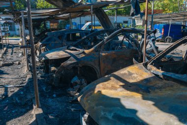 Kül ve çamur kaplı yanmış cesetlerde bükülmüş metal ve erimiş yapılar görülüyor. Arabanın içi mahvolmuş. Askeri çatışma ve bombardıman sonucu. Yıkılmış otopark.