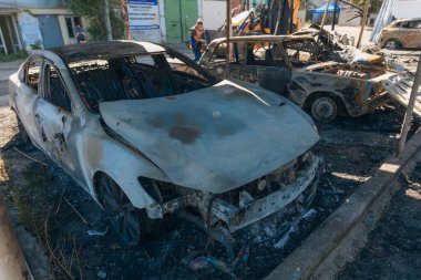 Kül ve çamur kaplı yanmış cesetlerde bükülmüş metal ve erimiş yapılar görülüyor. Arabanın içi mahvolmuş. Askeri çatışma ve bombardıman sonucu. Yıkılmış otopark.