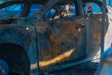 Kül ve çamur kaplı yanmış cesetlerde bükülmüş metal ve erimiş yapılar görülüyor. Arabanın içi mahvolmuş. Askeri çatışma ve bombardıman sonucu. Yıkılmış otopark.