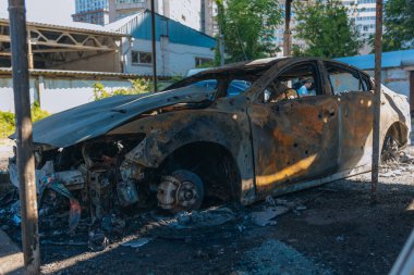 Kül ve çamur kaplı yanmış cesetlerde bükülmüş metal ve erimiş yapılar görülüyor. Arabanın içi mahvolmuş. Askeri çatışma ve bombardıman sonucu. Yıkılmış otopark.