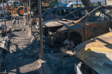 Kül ve çamur kaplı yanmış cesetlerde bükülmüş metal ve erimiş yapılar görülüyor. Arabanın içi mahvolmuş. Askeri çatışma ve bombardıman sonucu. Yıkılmış otopark.