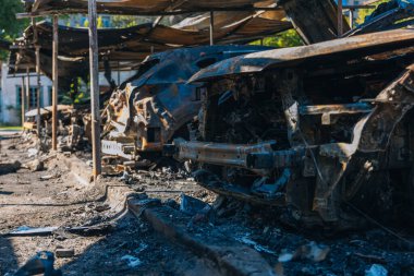 Kül ve çamur kaplı yanmış cesetlerde bükülmüş metal ve erimiş yapılar görülüyor. Arabanın içi mahvolmuş. Askeri çatışma ve bombardıman sonucu. Yıkılmış otopark.