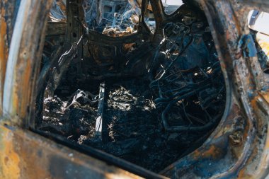 Kül ve çamur kaplı yanmış cesetlerde bükülmüş metal ve erimiş yapılar görülüyor. Arabanın içi mahvolmuş. Askeri çatışma ve bombardıman sonucu. Yıkılmış otopark.