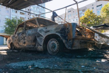 Kül ve çamur kaplı yanmış cesetlerde bükülmüş metal ve erimiş yapılar görülüyor. Arabanın içi mahvolmuş. Askeri çatışma ve bombardıman sonucu. Yıkılmış otopark.