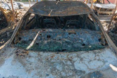 Kül ve çamur kaplı yanmış cesetlerde bükülmüş metal ve erimiş yapılar görülüyor. Arabanın içi mahvolmuş. Askeri çatışma ve bombardıman sonucu. Yıkılmış otopark.