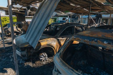 Kül ve çamur kaplı yanmış cesetlerde bükülmüş metal ve erimiş yapılar görülüyor. Arabanın içi mahvolmuş. Askeri çatışma ve bombardıman sonucu. Yıkılmış otopark.