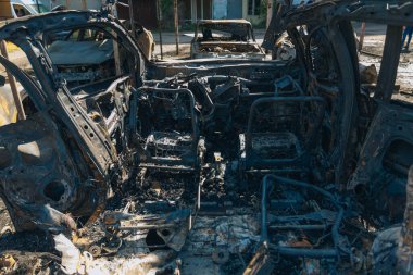 Kül ve çamur kaplı yanmış cesetlerde bükülmüş metal ve erimiş yapılar görülüyor. Arabanın içi mahvolmuş. Askeri çatışma ve bombardıman sonucu. Yıkılmış otopark.