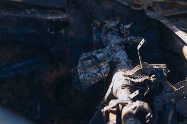 Kül ve çamur kaplı yanmış cesetlerde bükülmüş metal ve erimiş yapılar görülüyor. Arabanın içi mahvolmuş. Askeri çatışma ve bombardıman sonucu. Yıkılmış otopark.