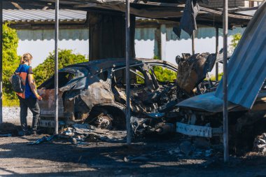 Kül ve çamur kaplı yanmış cesetlerde bükülmüş metal ve erimiş yapılar görülüyor. Arabanın içi mahvolmuş. Askeri çatışma ve bombardıman sonucu. Yıkılmış otopark.