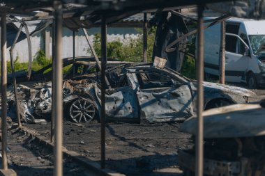 Kül ve çamur kaplı yanmış cesetlerde bükülmüş metal ve erimiş yapılar görülüyor. Arabanın içi mahvolmuş. Askeri çatışma ve bombardıman sonucu. Yıkılmış otopark.