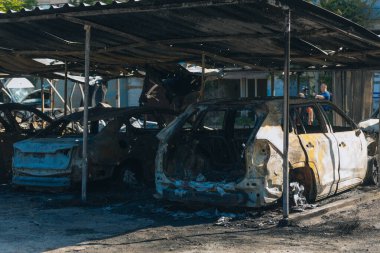 Kül ve çamur kaplı yanmış cesetlerde bükülmüş metal ve erimiş yapılar görülüyor. Arabanın içi mahvolmuş. Askeri çatışma ve bombardıman sonucu. Yıkılmış otopark.