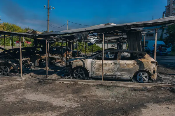 Kül ve çamur kaplı yanmış cesetlerde bükülmüş metal ve erimiş yapılar görülüyor. Arabanın içi mahvolmuş. Askeri çatışma ve bombardıman sonucu. Yıkılmış otopark.