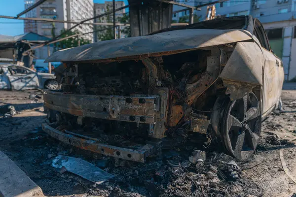 Kül ve çamur kaplı yanmış cesetlerde bükülmüş metal ve erimiş yapılar görülüyor. Arabanın içi mahvolmuş. Askeri çatışma ve bombardıman sonucu. Yıkılmış otopark.